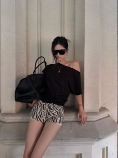 Woman in zebra print shorts and an off-shoulder top leaning against a wall