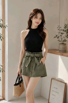 Woman in a black halter top and olive green shorts holding a straw bag indoors