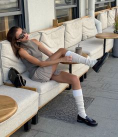 Woman in a sleeveless top and pleated skirt with leg warmers sitting outdoors