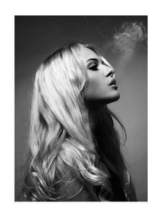 Woman with long blonde curly hair in a black and white profile shot with smoke