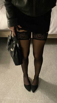 Person in a black leather jacket, skirt, and lace-top stockings indoors