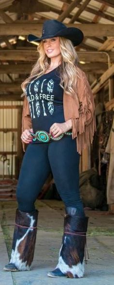 Woman in a cowboy hat, fringe jacket, and fur boots posing in a barn