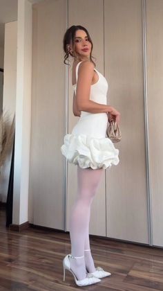 Woman in a white ruffle dress and white tights holding a small handbag