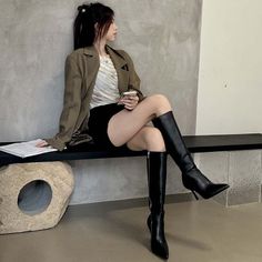Woman in a blazer, black shorts, and knee-high boots sitting indoors