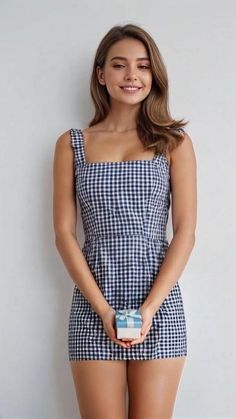 Woman in a gingham dress holding a small gift box, smiling at the camera