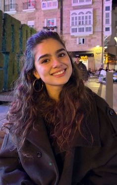 Smiling woman with long curly hair and hoop earrings at night outdoors