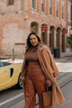 Woman in a long brown coat and leather pants on a city street