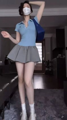 Person in a blue polo shirt and gray pleated skirt wearing a face mask indoors