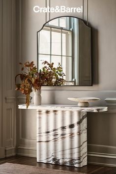 A marble console table with a mirror and dried flowers in a neutral-toned room