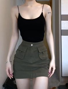 Woman in a black camisole and olive mini skirt with a tattoo on her arm