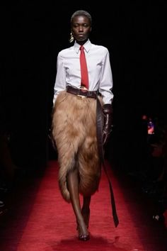 Model in a fur skirt, white shirt, and red tie on a red runway