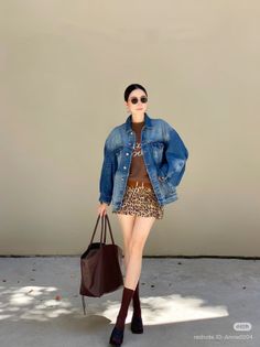 Woman in a denim jacket and leopard print skirt holding a brown tote bag outdoors