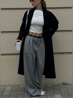 Woman in a black coat, crop top, and wide leg pants holding a coffee cup