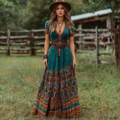 Woman in a maxi dress and cowboy hat standing in a grassy outdoor setting