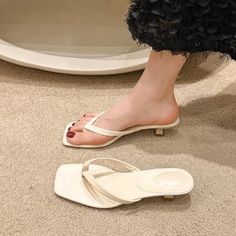Foot wearing a white sandal with red nail polish, another sandal on the carpet