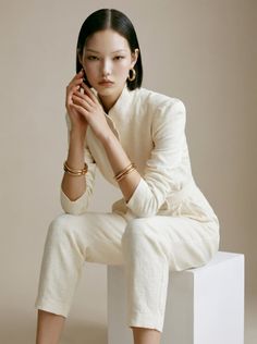 Woman with short dark hair wearing a cream jumpsuit and gold jewelry