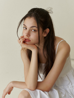 Young woman with long dark hair and a white dress, looking at the camera