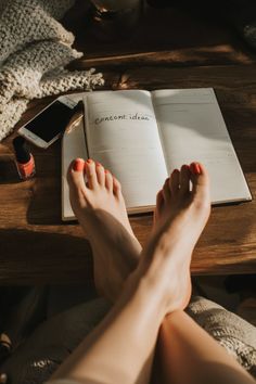 Crossed feet with orange nail polish on a wooden table with a notebook