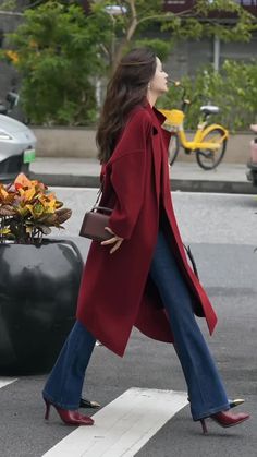 Woman in a red coat and flared jeans walking on a street