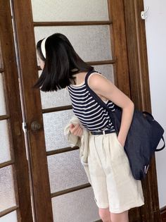 Woman with short black hair wearing a striped top and beige shorts indoors
