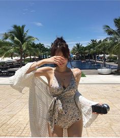 Woman in a floral swimsuit and long cardigan by a swimming pool