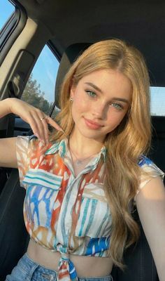 Young woman with blonde hair and blue eyes wearing a colorful crop top in a car