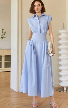 Woman in a light blue dress holding a white handbag indoors