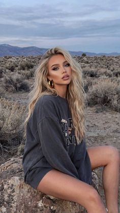 Woman with long blonde hair wearing an oversized sweatshirt in a desert landscape