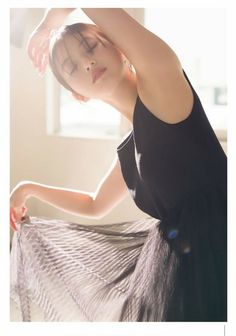Woman in a black dress with closed eyes and arms raised in soft indoor lighting