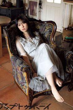 Woman with long dark hair in a light dress sitting barefoot in an ornate armchair