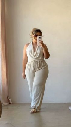 Woman in a light-colored halter top and wide-leg pants taking a mirror selfie