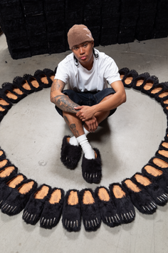 Person wearing bear claw slippers and a beanie, surrounded by more slippers