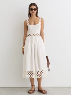 Woman in a white dress with cut-out details and sunglasses standing indoors