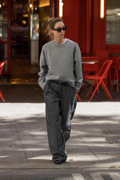 Woman in a grey sweater and wide leg pants walking on a street