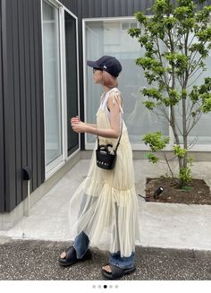 Person in a sheer dress over jeans and a baseball cap outdoors