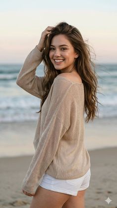 Smiling woman with long hair in a sweater and white shorts on a beach