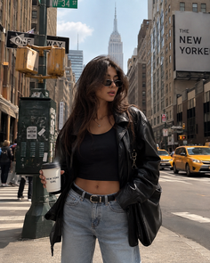 Woman in a leather jacket and crop top on a city street with the Empire State Building in the background