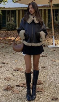 Woman in a shearling jacket and black skirt standing outdoors with autumn leaves