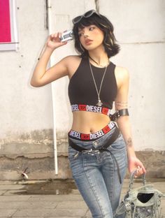 Woman in a crop top and jeans holding a digital camera outdoors