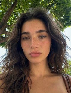 Woman with long brown hair and freckles outdoors under green trees