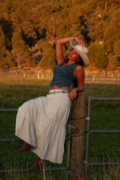 Woman in a cowboy hat and denim vest posing on a fence at golden hour