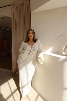 Woman in a white knit dress leaning against a wall with soft lighting