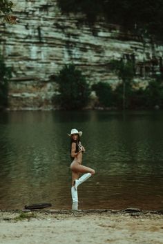 Woman in a cowboy hat and boots posing in a lake with a rocky cliff background