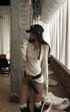 Woman in a baseball cap and long sleeve shirt drinking a beverage indoors