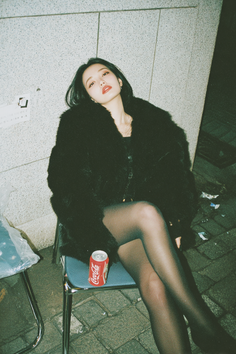 Woman in a black fur coat and tights sitting outdoors at night