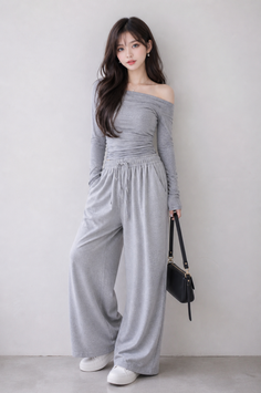 Woman in a gray off-shoulder top and wide-leg pants with a black handbag
