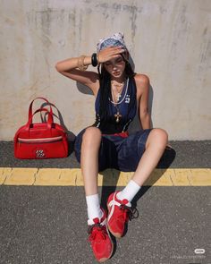 Woman in a bandana and denim shorts sitting on asphalt with a red bag