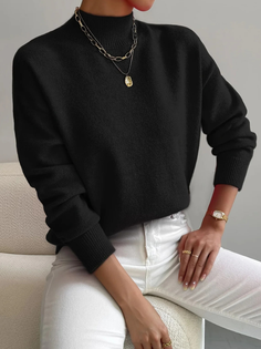 Person in a black sweater and white pants with gold jewelry