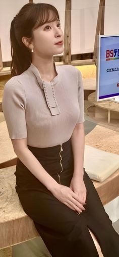 Woman with a ponytail wearing a ribbed top and black skirt indoors