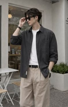 Man in a dark shirt and khaki pants adjusting his sunglasses outdoors